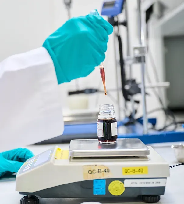 CAREANDD-labo Une personne en gants bleus manipule une pipette au-dessus d'un flacon sur une balance dans un laboratoire.